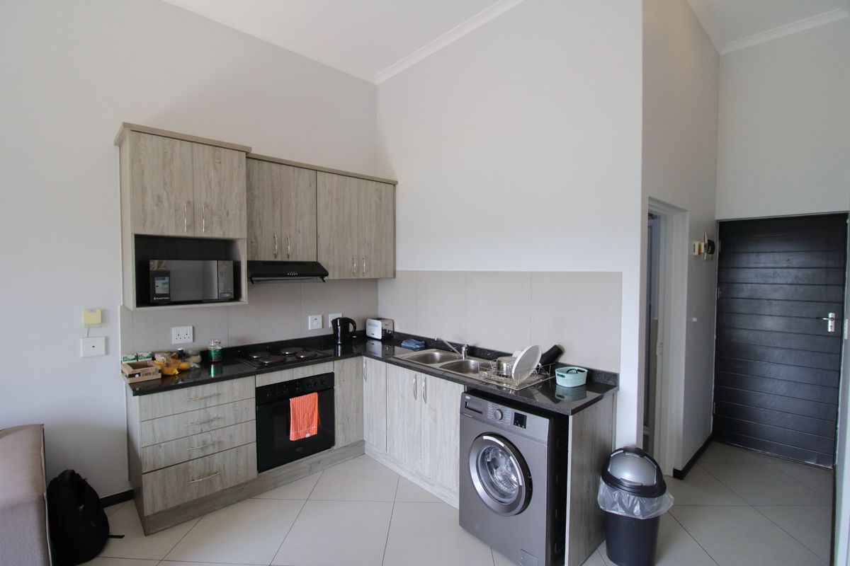 Compact modern kitchen featuring light wood-grain cabinetry, granite countertops, integrated oven, hob, extractor fan, and space for a washing machine.