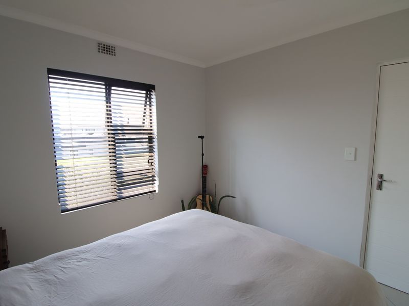 A clean and neutral bedroom featuring a window with venetian blinds and a standard internal door.