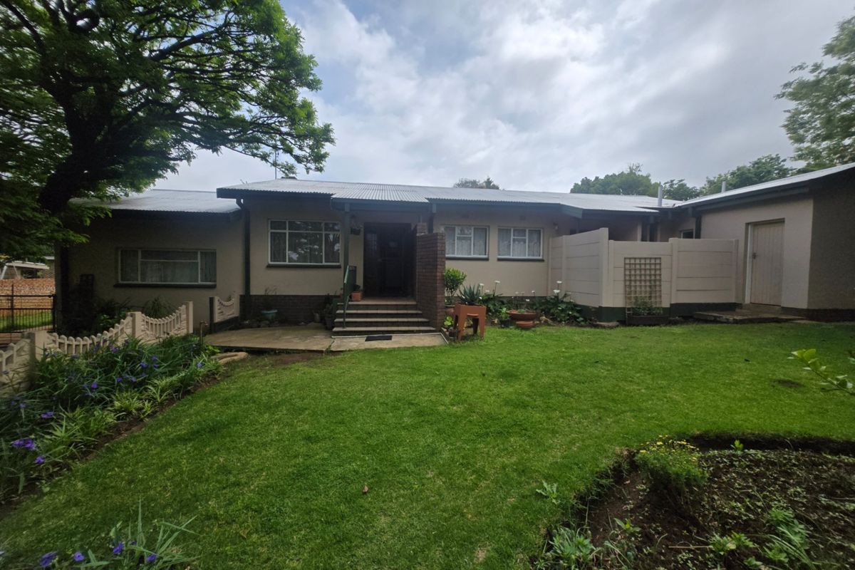A view of the rear exterior of the house featuring a corrugated metal roof, brick facade, concrete patio, and a well-maintained garden.