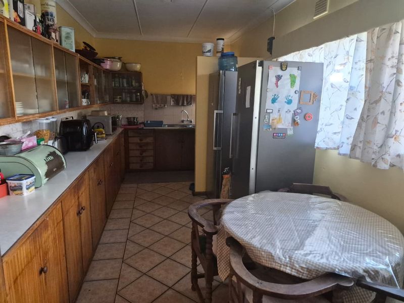 A functional kitchen featuring extensive wooden cabinetry, laminate countertops, a double sink, and tiled flooring, offering potential for a modern renovation.