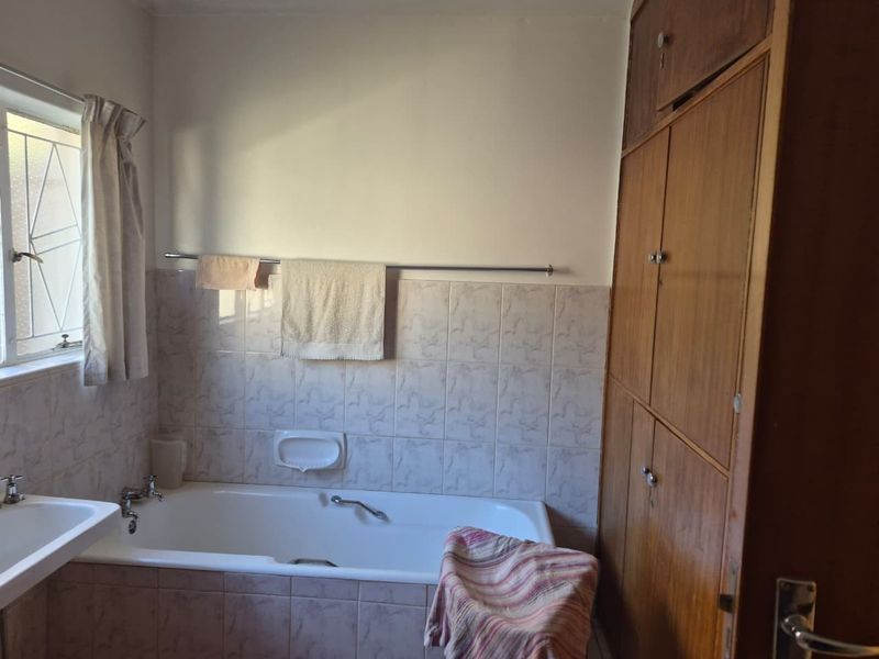 A dated bathroom featuring a built-in bathtub, wall-mounted basin, and floor-to-ceiling wooden storage cabinetry with tiled splashbacks.