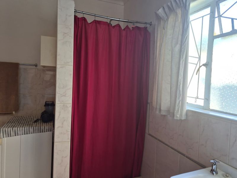 A functional bathroom featuring tiled walls, a shower area with a curtain, and a basin with a window providing natural light.