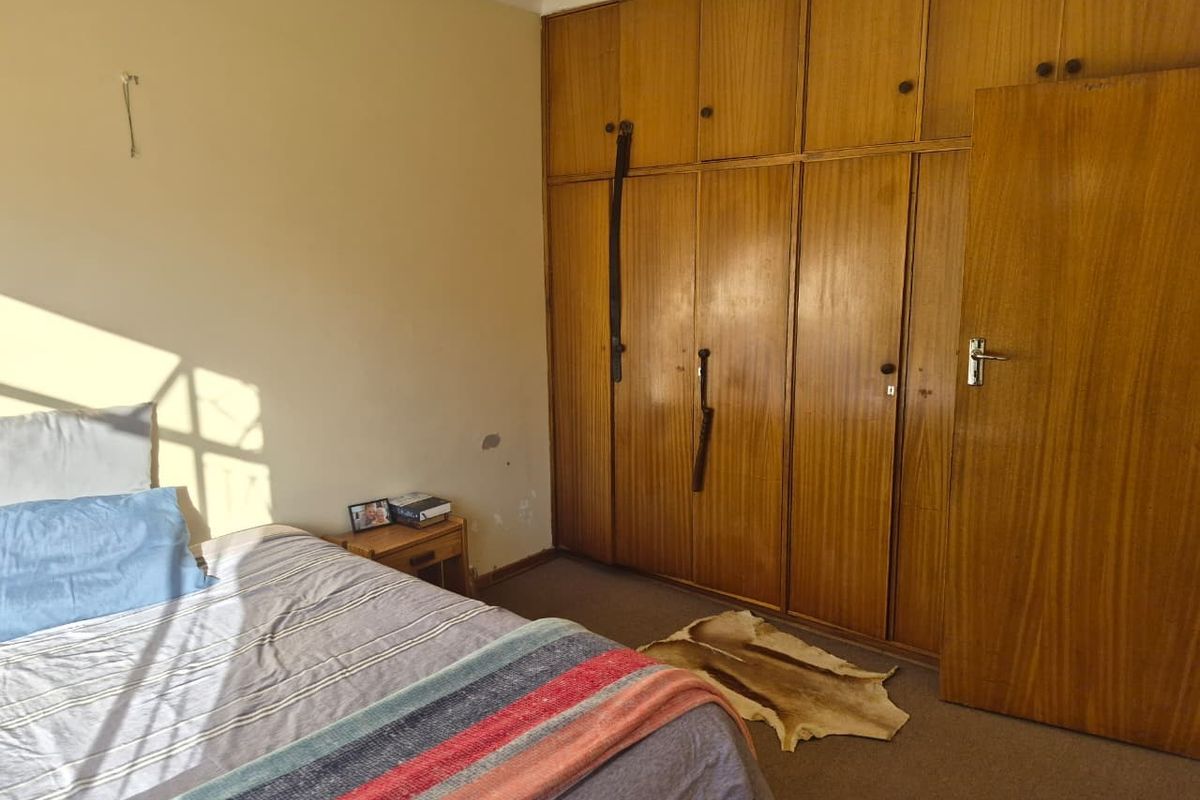 A bedroom featuring floor-to-ceiling built-in wooden cupboards and carpeted flooring, requiring minor cosmetic updates to the walls and finishes.