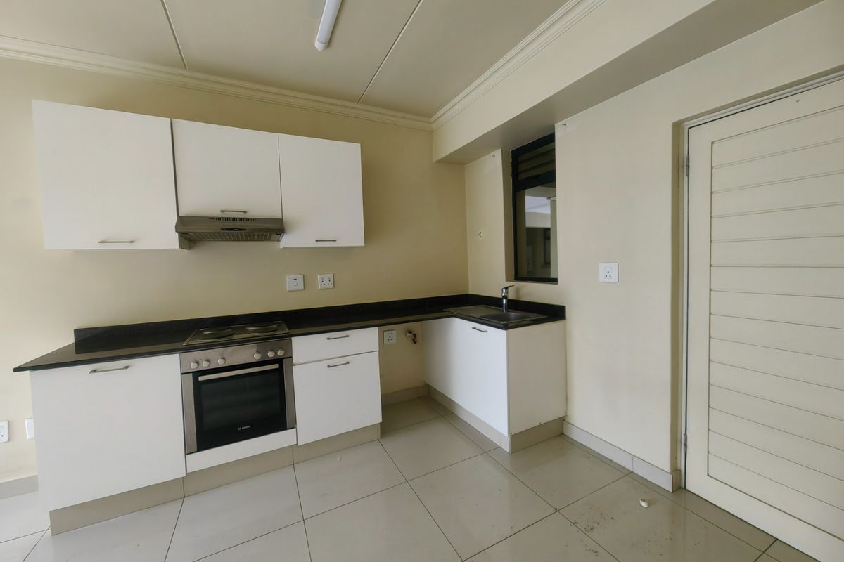 A functional kitchen featuring white cabinetry, granite countertops, a built-in oven, hob, extractor fan, and tiled flooring.