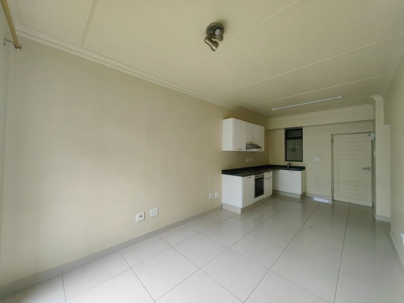 An open-plan living and kitchen area featuring tiled flooring, built-in cabinetry, and integrated kitchen appliances in a clean, neutral space.