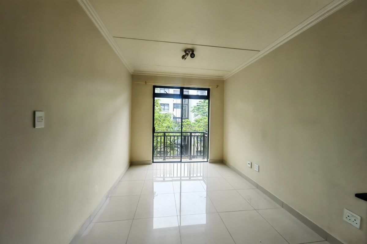 A bright, empty living area featuring neutral walls, polished tiled flooring, and a sliding glass door leading to a private balcony.