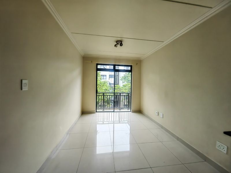 A bright, empty living area featuring neutral walls, polished tiled flooring, and a sliding glass door leading to a private balcony.