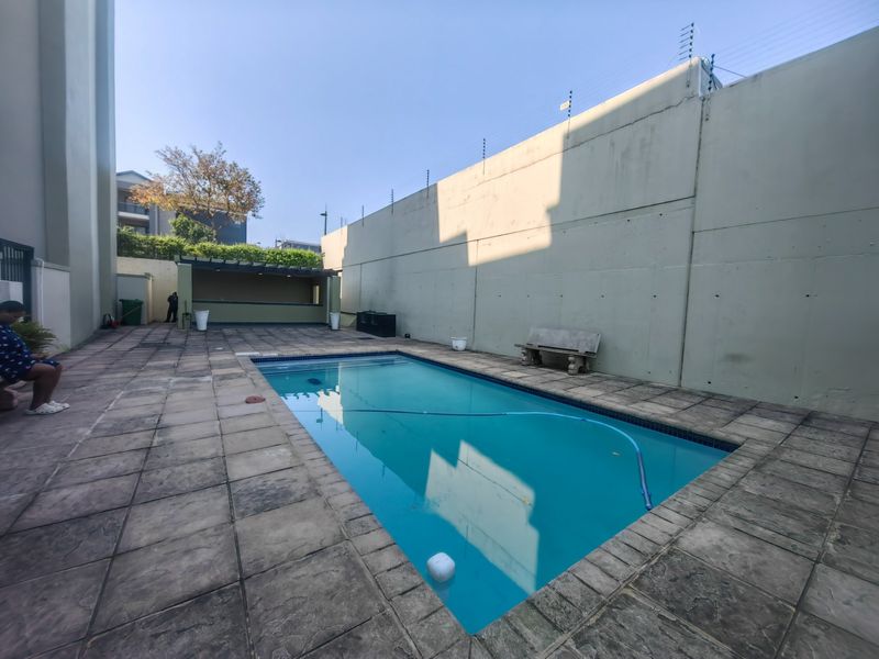 Outdoor pool area featuring a rectangular swimming pool, paved surround, perimeter wall with electric fencing, and a covered bar structure.