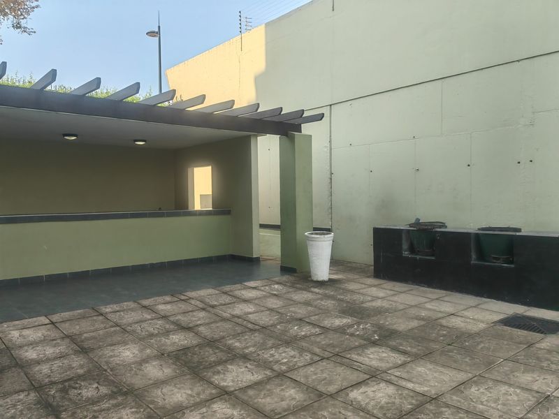 Outdoor patio area featuring a covered pergola, built-in bar counter, and a dedicated built-in braai station with tiled flooring.