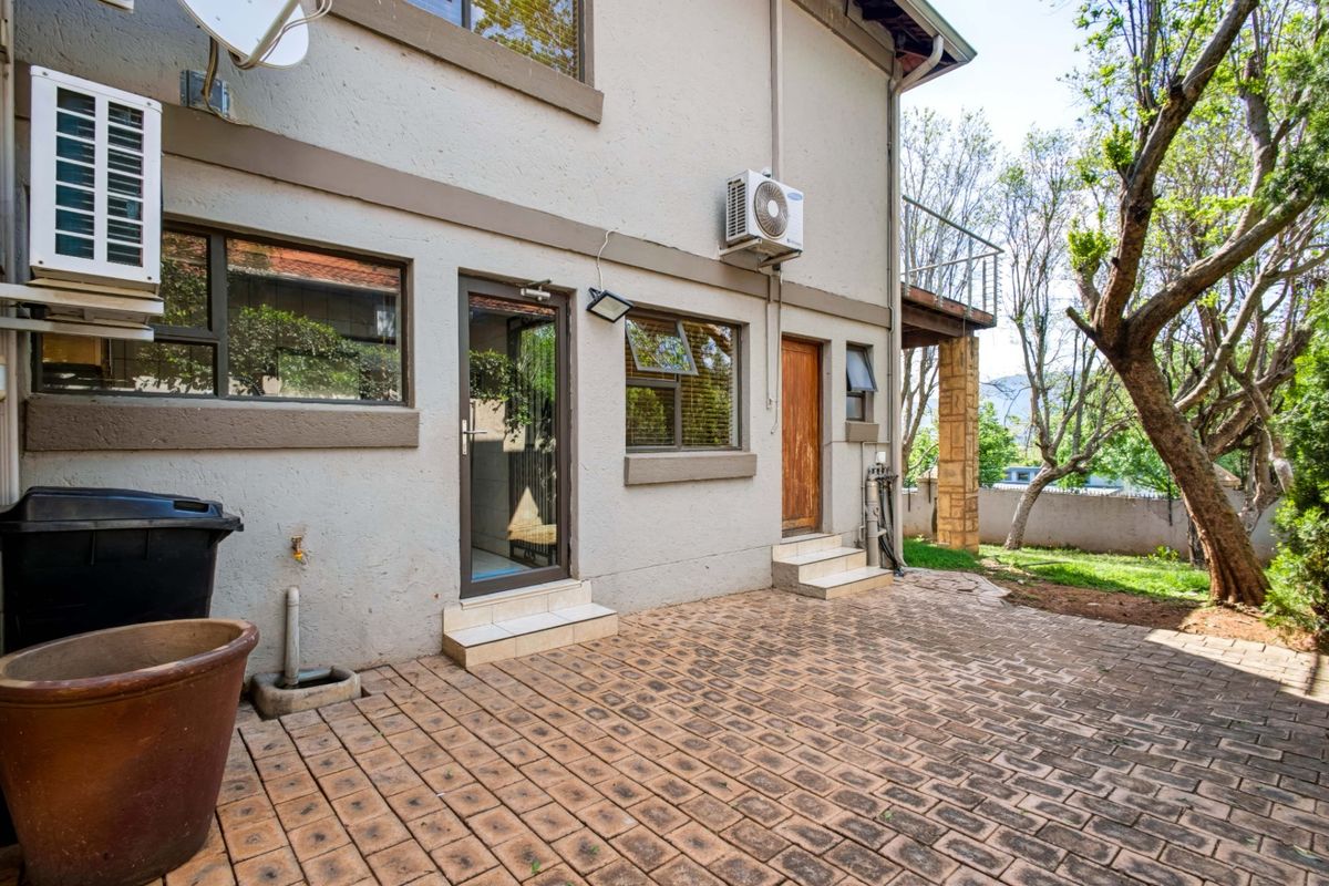 Rear exterior view featuring a paved patio area, multiple access points, and an elevated timber balcony with stone support detailing.