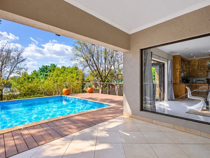 Covered patio area featuring tiled flooring, overlooking a swimming pool and wooden deck with views of the surrounding garden.