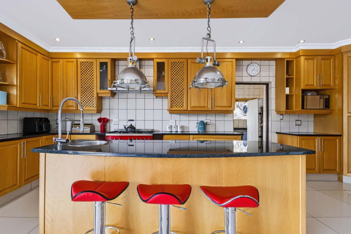 A spacious kitchen featuring warm wooden cabinetry, granite countertops, a central island with breakfast bar seating, and integrated gas cooking appliances.