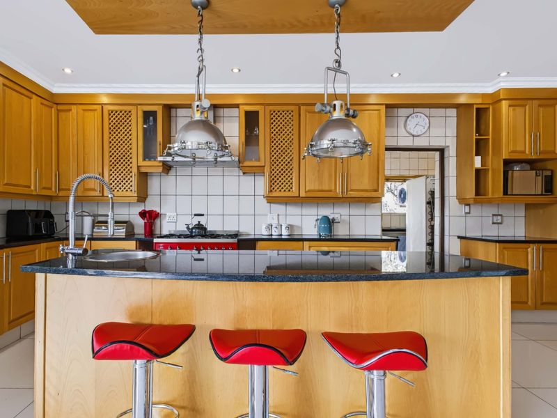A spacious kitchen featuring warm wooden cabinetry, granite countertops, a central island with breakfast bar seating, and integrated gas cooking appliances.
