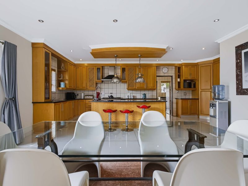 Spacious open-plan kitchen featuring warm wooden cabinetry, granite countertops, a central island, and modern recessed lighting, seamlessly integrated with the dining area.