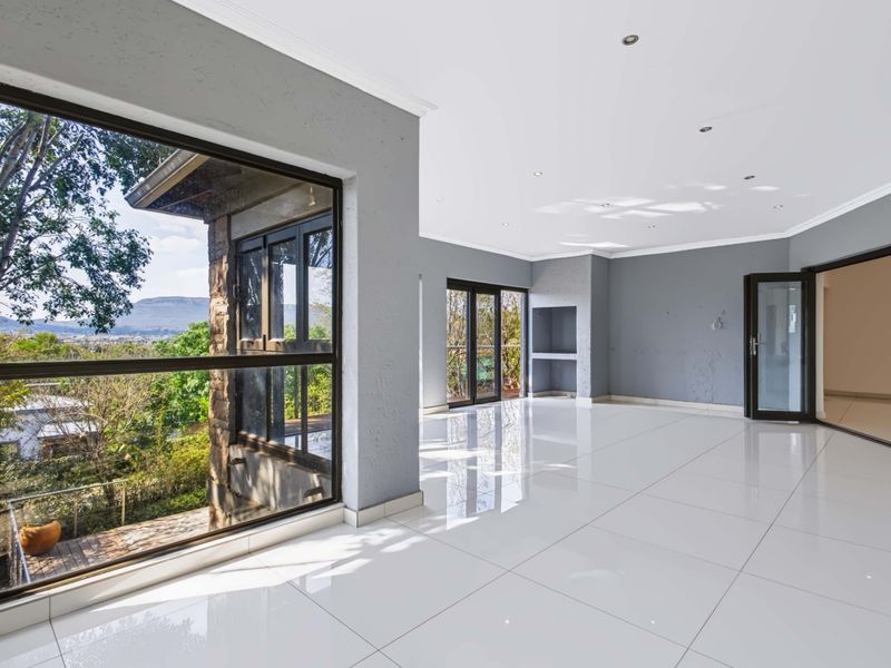 Spacious, light-filled living area featuring large format white porcelain tiles, recessed lighting, and expansive windows offering scenic views.