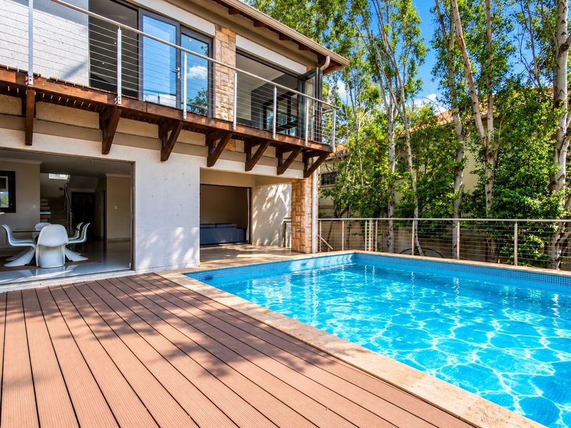 A well-maintained outdoor pool area featuring timber decking, stone accents, and a stainless steel balustrade, seamlessly connecting to the indoor living space.
