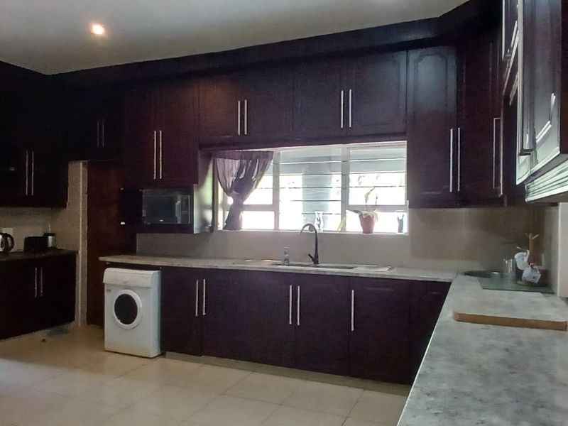 A functional kitchen featuring dark wood cabinetry, laminate countertops, built-in oven, and tiled flooring with ample storage space.