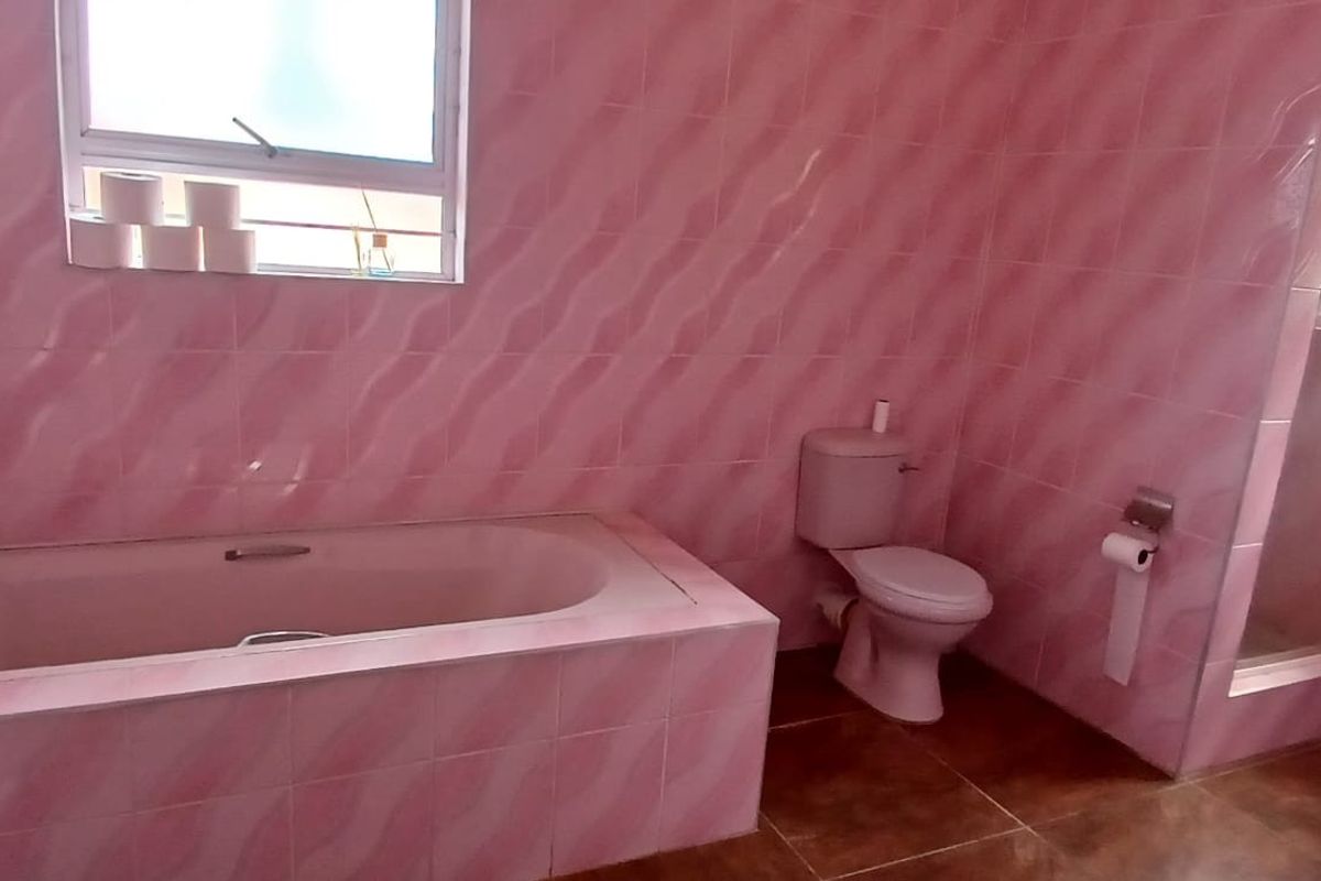 A spacious bathroom featuring a built-in bathtub, separate shower enclosure, toilet, and pedestal basin with pink wall tiling.