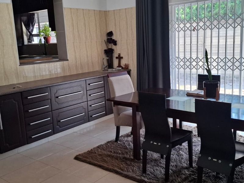 Dining area featuring built-in dark wood cabinetry, tiled flooring, and a pass-through window connecting to the kitchen, with access to the exterior via security gate.