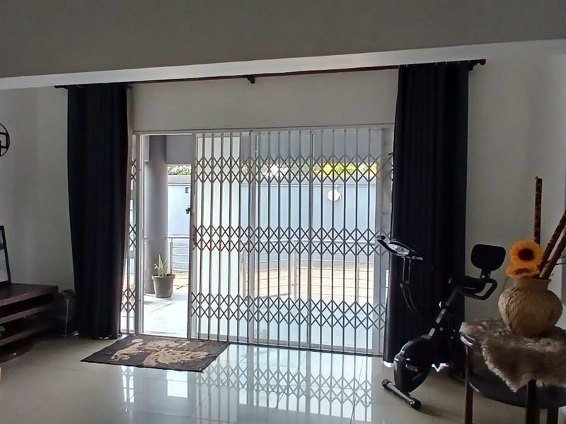 Living room area featuring tiled flooring, a glass block window, and a sliding door with a security gate leading to the exterior.