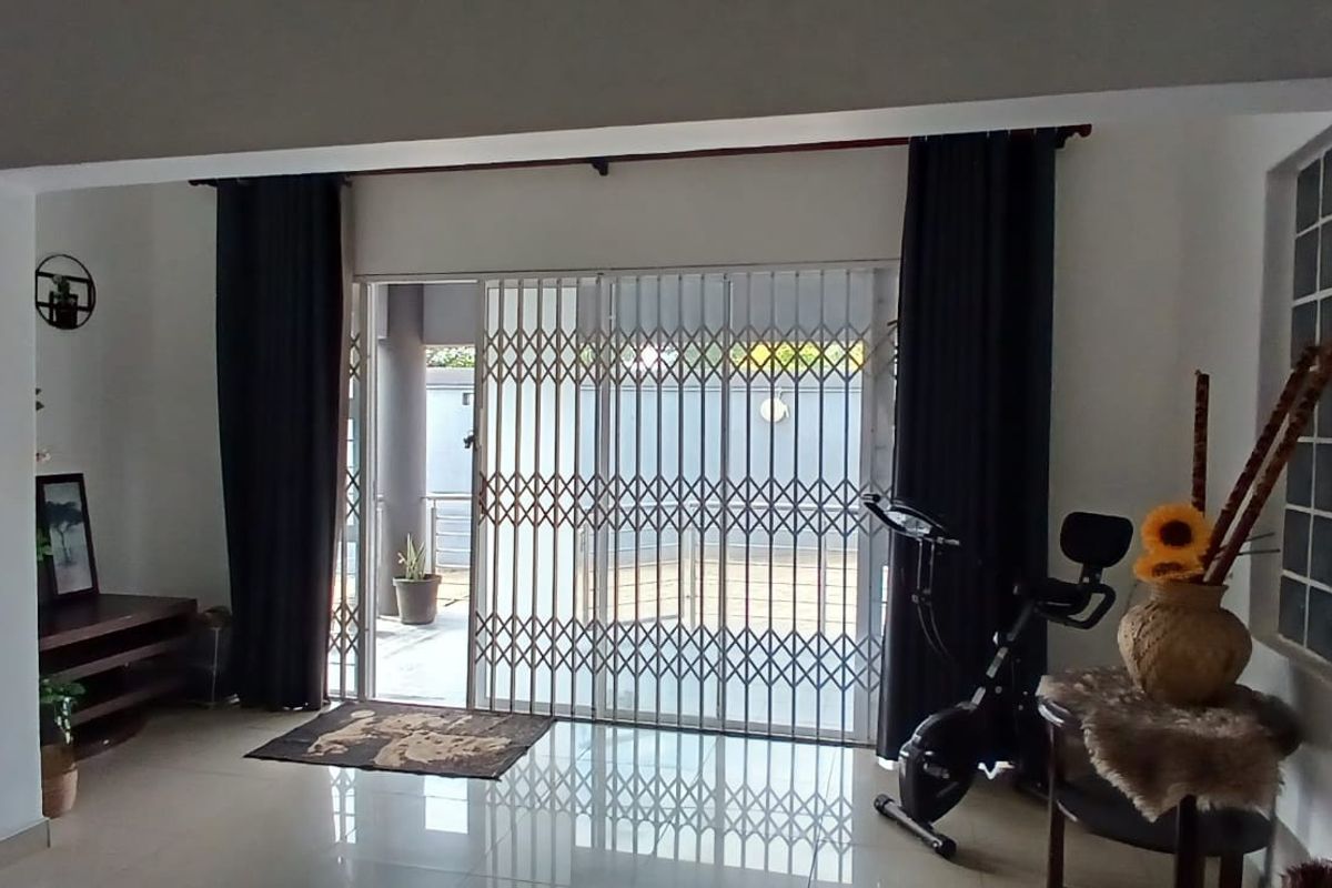 Living room area featuring tiled flooring, a glass block window, and a sliding door with a security gate leading to the exterior.