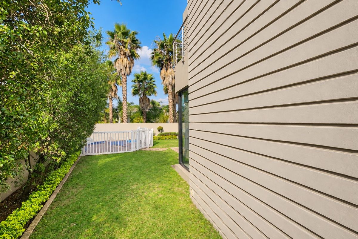 A well-maintained rear garden featuring horizontal timber cladding on the building exterior, a manicured lawn, and a fenced swimming pool area.
