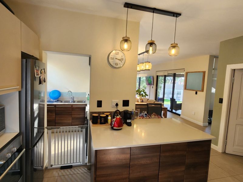 Open plan kitchen featuring a central island with stone countertop, modern cabinetry, built-in appliances, and pendant lighting, flowing into the adjacent living area.