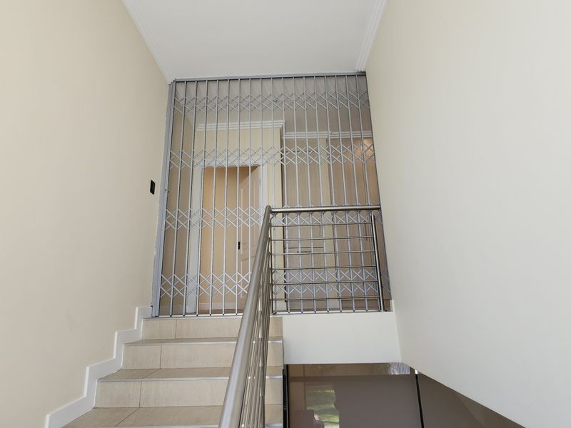 A bright hallway featuring a staircase with a stainless steel balustrade and a secure metal gate at the top of the landing.