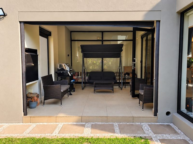 A covered patio area featuring tiled flooring and a built-in braai, seamlessly connecting to the interior living space through large sliding glass doors.