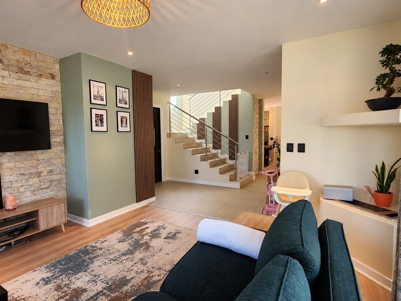 Modern open-plan living area featuring a stone accent wall, timber slat detailing, and a contemporary staircase with stainless steel railings.