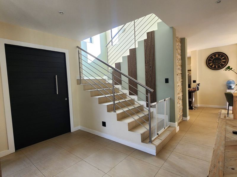 Modern entrance hall featuring a tiled staircase with stainless steel balustrades, decorative timber slat paneling, and a stone feature wall.