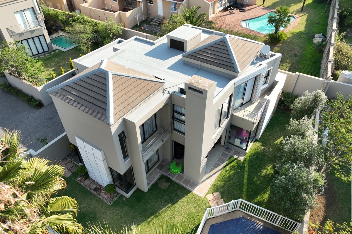 Aerial view of a modern two-story residential property featuring a tiled roof, chimney, balcony, and a private swimming pool set within a landscaped garden.
