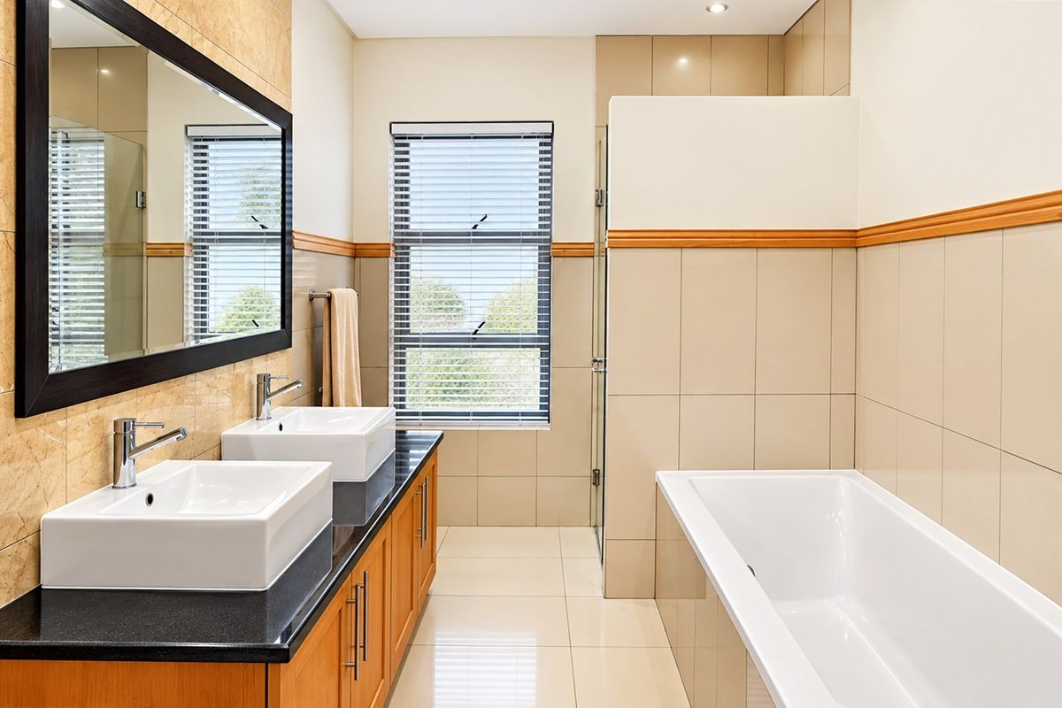 Modern bathroom featuring a double vanity with vessel sinks, a built-in bathtub, and a separate glass-enclosed shower with neutral tiling.
