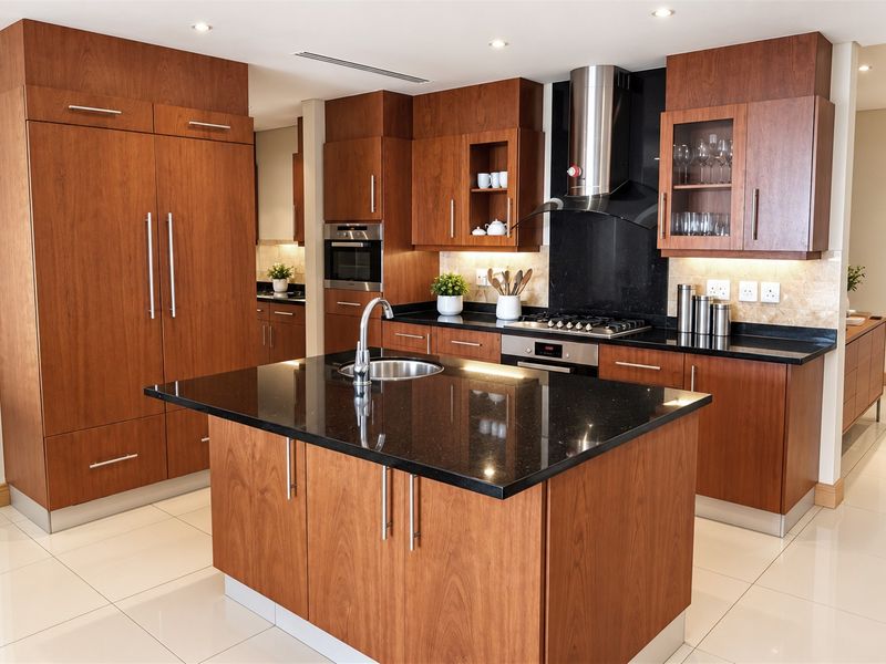 Modern kitchen featuring rich wood cabinetry, black granite countertops, a central island with sink, and integrated stainless steel appliances.
