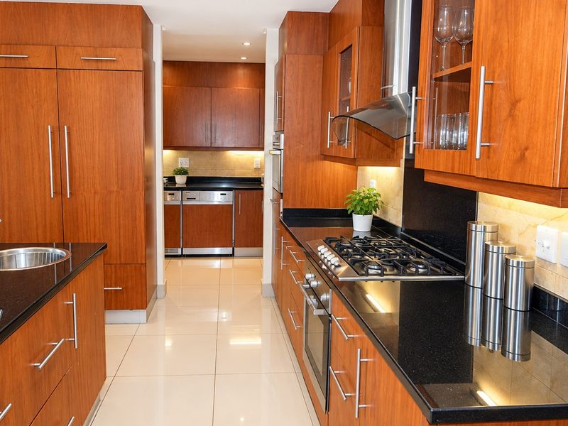 Modern kitchen featuring warm wood cabinetry, sleek black granite countertops, integrated appliances, gas hob, and polished tile flooring with under-cabinet lighting.