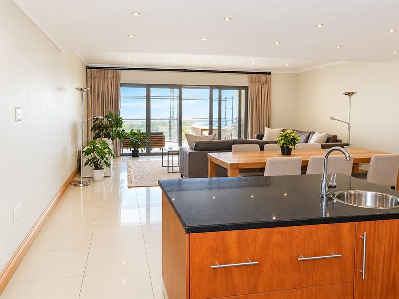 Spacious open-plan living and dining area featuring a modern kitchen island with granite countertops, tiled floors, and large sliding doors leading to a balcony.