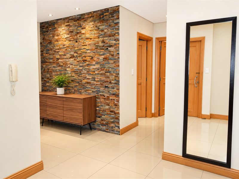 A well-maintained hallway featuring a decorative stone feature wall, polished tile flooring, and recessed downlighting, providing a clean and modern entrance area.
