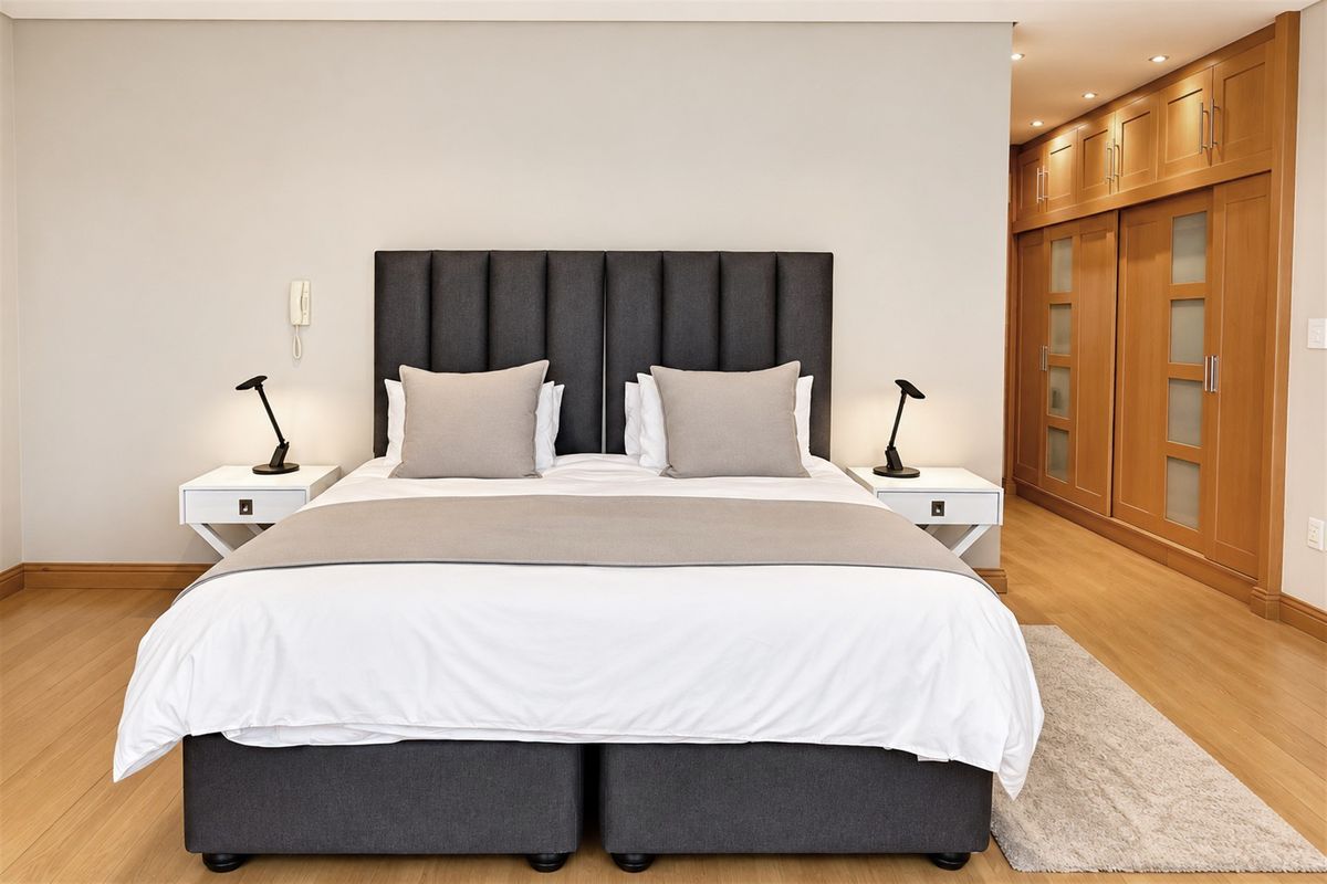 A well-maintained bedroom featuring light laminate flooring, recessed ceiling lighting, and extensive built-in wooden cabinetry for storage.