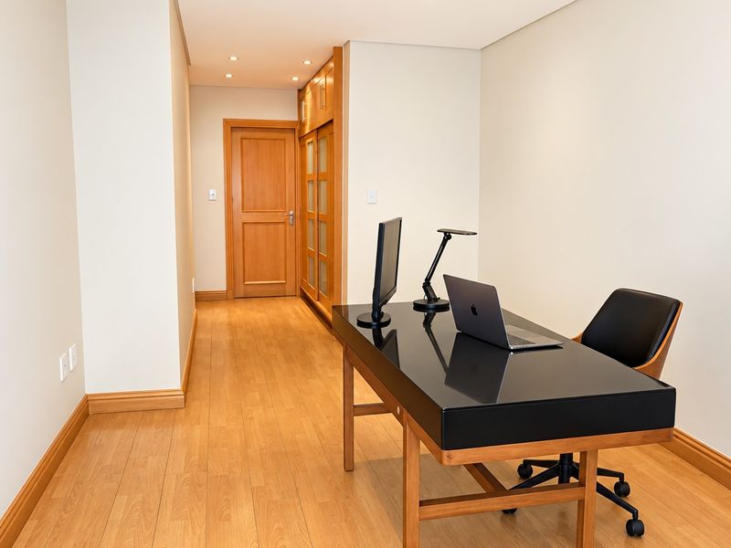 A well-maintained home office featuring warm wooden flooring, recessed lighting, and integrated built-in cabinetry for storage.