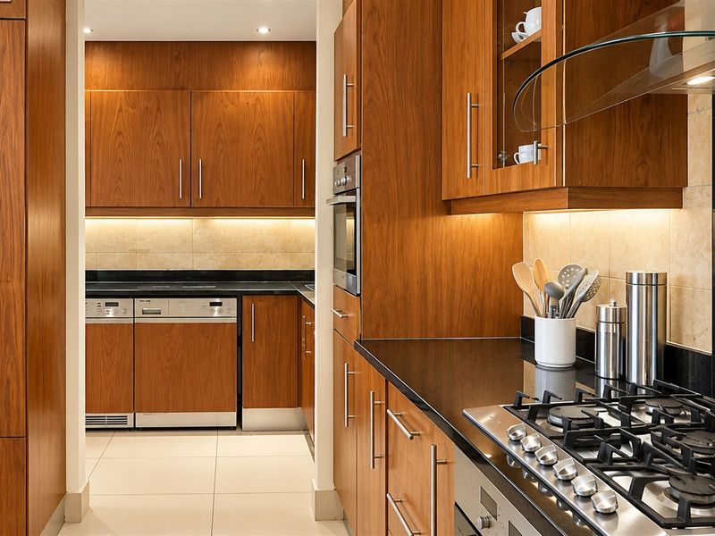 Modern kitchen featuring warm wooden cabinetry, sleek black granite countertops, integrated appliances, and a gas cooktop with a glass extractor hood.