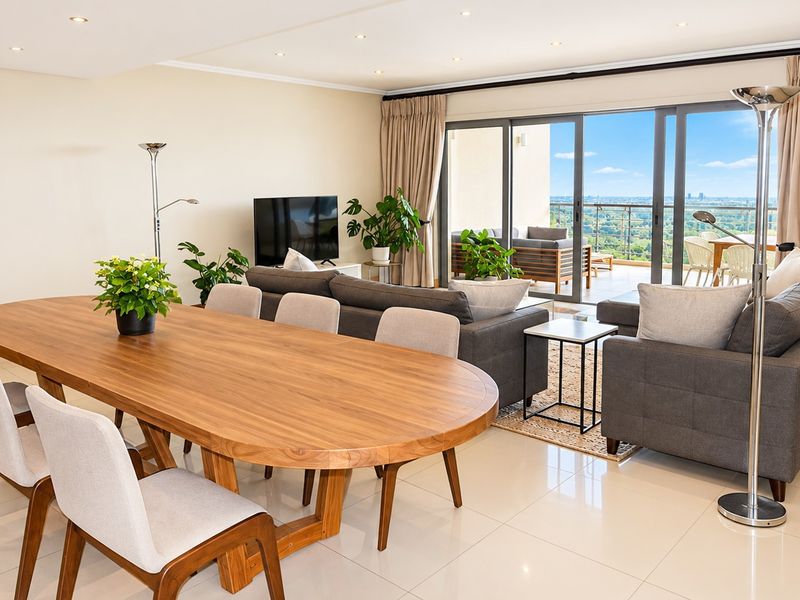Spacious open-plan living and dining area featuring large sliding glass doors that open onto a balcony with expansive views.