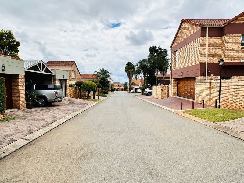 A view of a residential street featuring brick-faced houses with tiled roofs, paved driveways, and established landscaping in a suburban estate setting.
