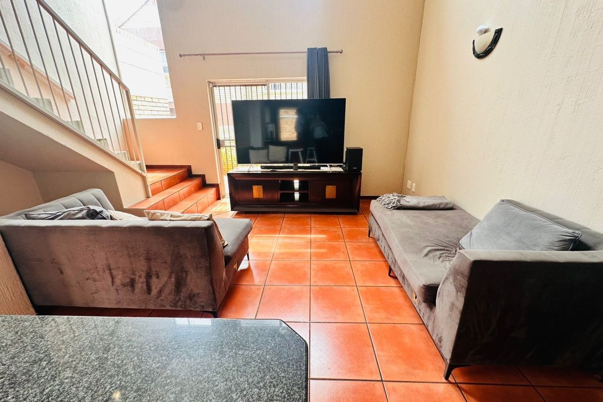Spacious living room featuring terracotta floor tiles, a staircase with a metal balustrade, and a sliding glass door leading to the exterior.
