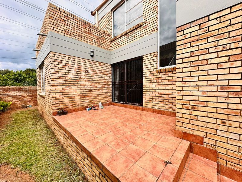 A paved outdoor patio area featuring face-brick construction, a security gate entrance, and direct access to the surrounding garden space.