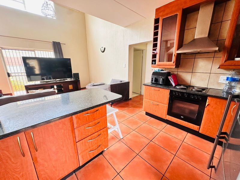 Open-plan kitchen and living area featuring wooden cabinetry, granite countertops, built-in oven and hob, and tiled flooring throughout.
