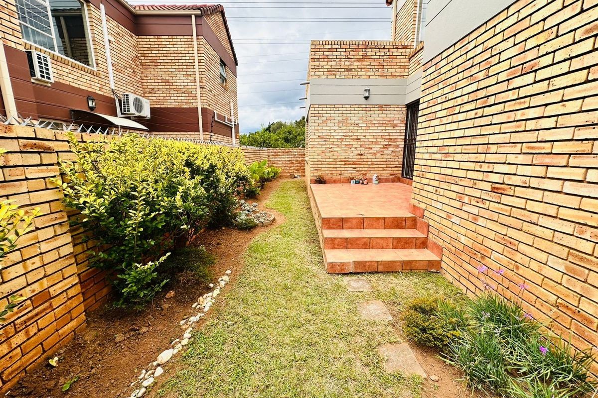 A view of the rear exterior featuring a brick-paved patio, a small lawn area, and brick boundary walls with security features.