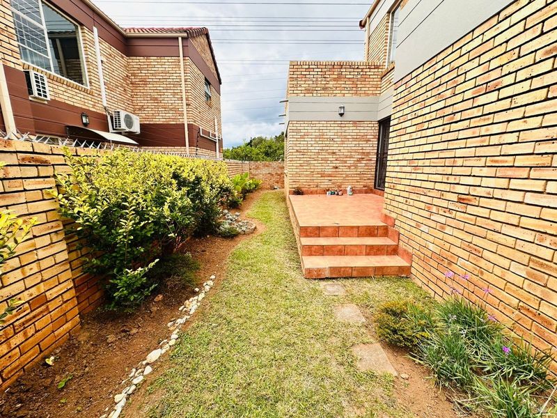 A view of the rear exterior featuring a brick-paved patio, a small lawn area, and brick boundary walls with security features.
