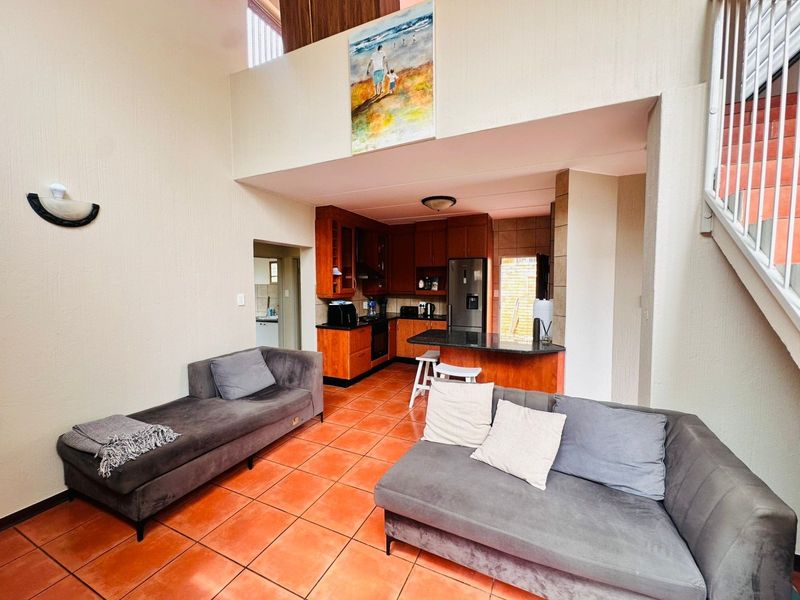 Open-plan living area featuring terracotta floor tiles, a double-volume ceiling, and a functional kitchen with wooden cabinetry and granite countertops.