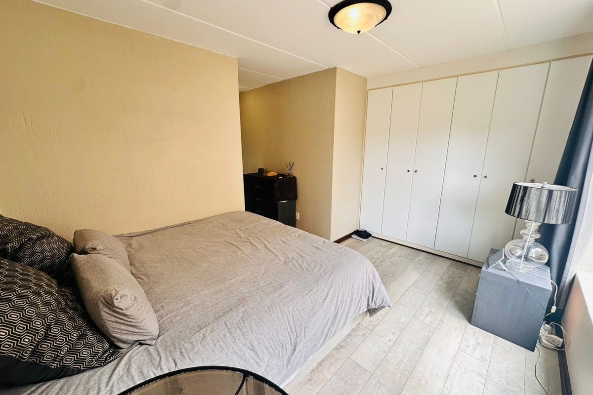 A bedroom featuring light-toned laminate flooring and a large built-in wardrobe with white cabinetry.