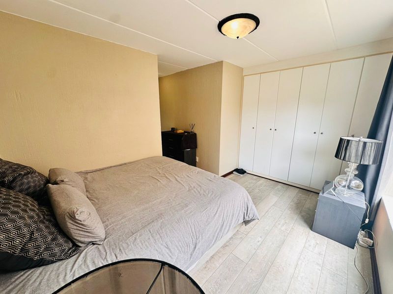 A bedroom featuring light-toned laminate flooring and a large built-in wardrobe with white cabinetry.